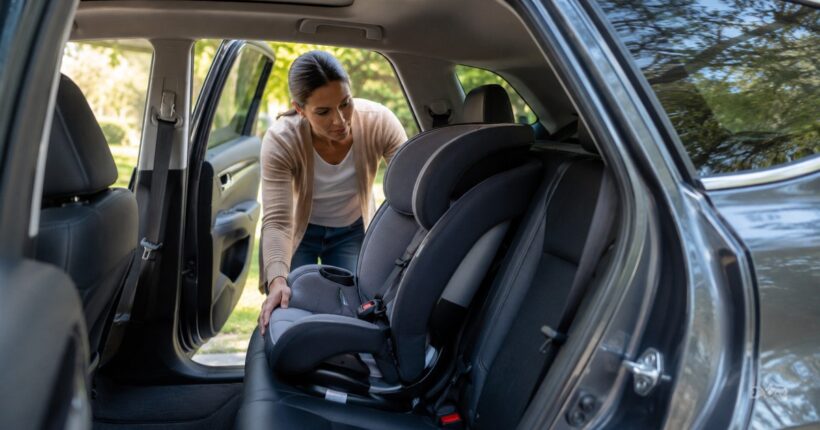 Parent checks the back seat of a parked vehicle with an empty child car seat visible before locking the car.