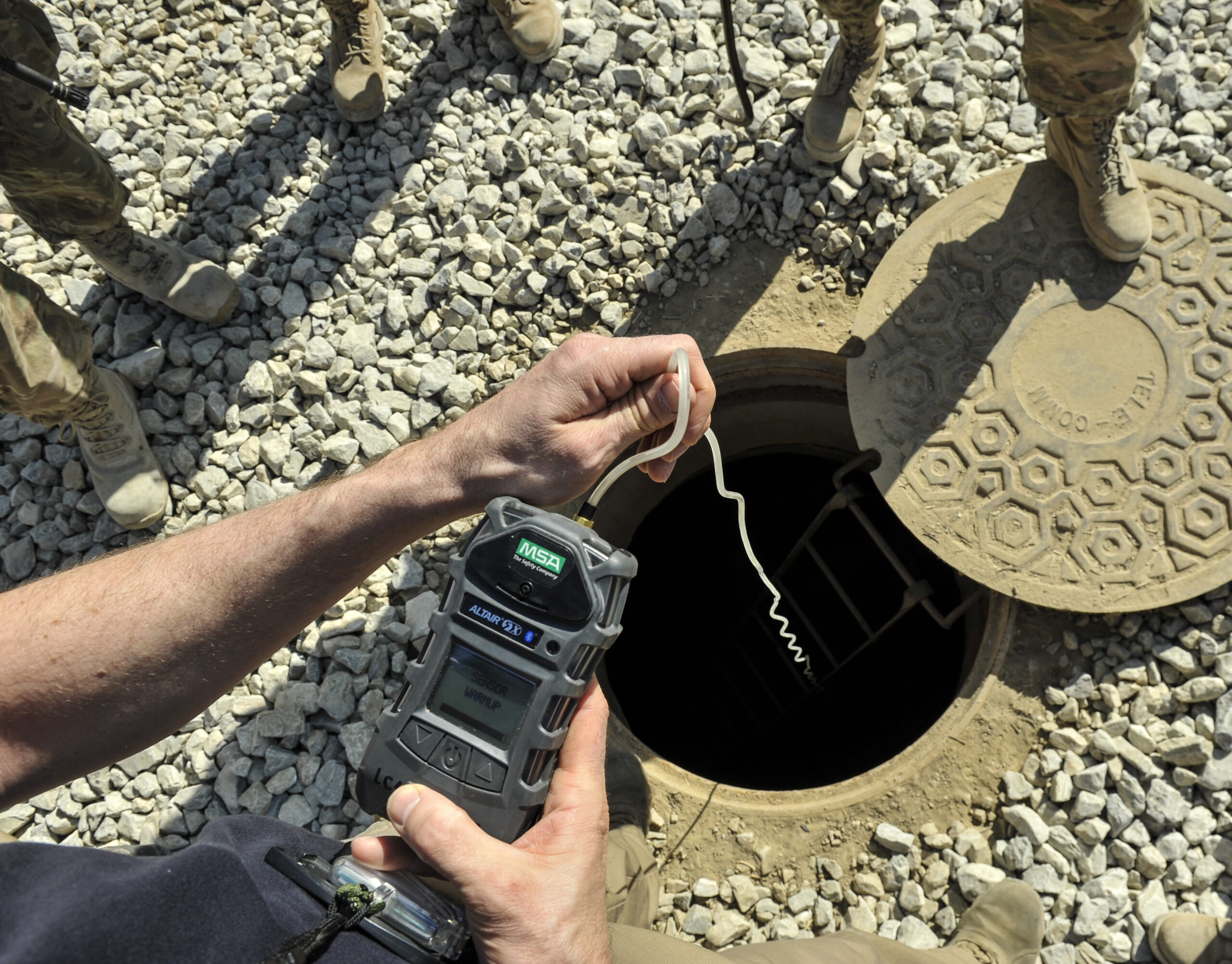 Worker using a portable gas monitor to test the atmosphere at a manhole before confined space work.