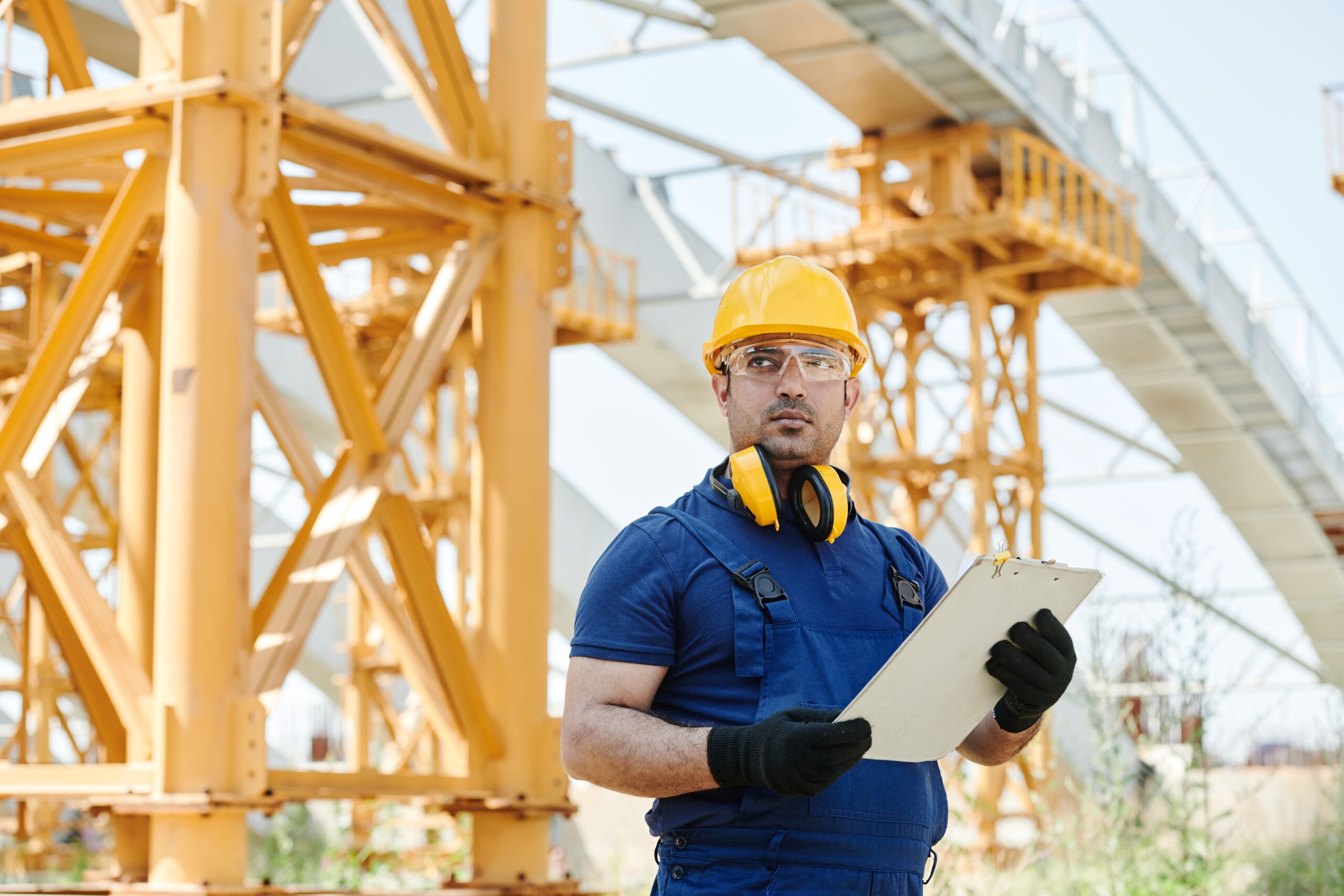 Construction worker wearing a hard hat and safety glasses conducting a jobsite inspection with a clipboard